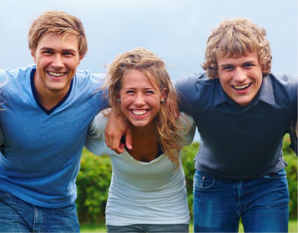 Drei junge Erwachsene lachen Arm in Arm in die Kamera